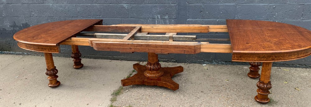 An extended Victorian pollard oak dining table featuring carved columnar legs, a central pedestal base, and a figured wood grain top. View XIII