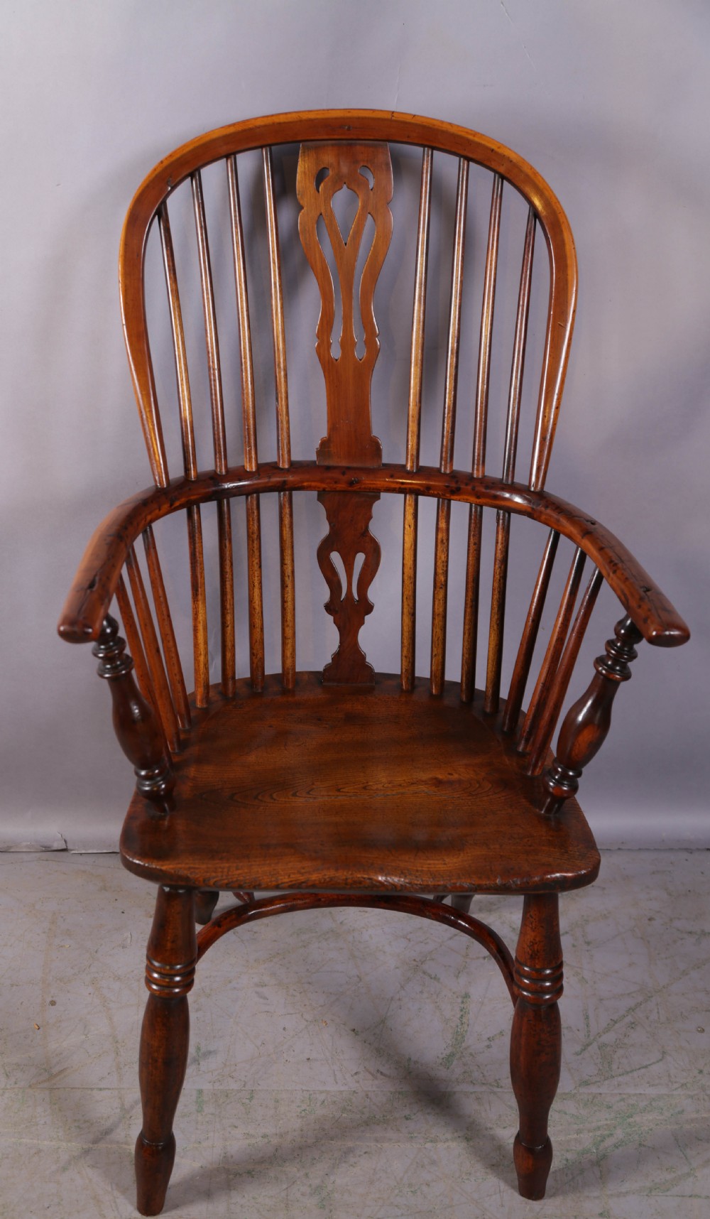 An antique yew wood high back Windsor armchair featuring a pierced central splat, spindled hoop back, turned legs, and a solid shaped seat.