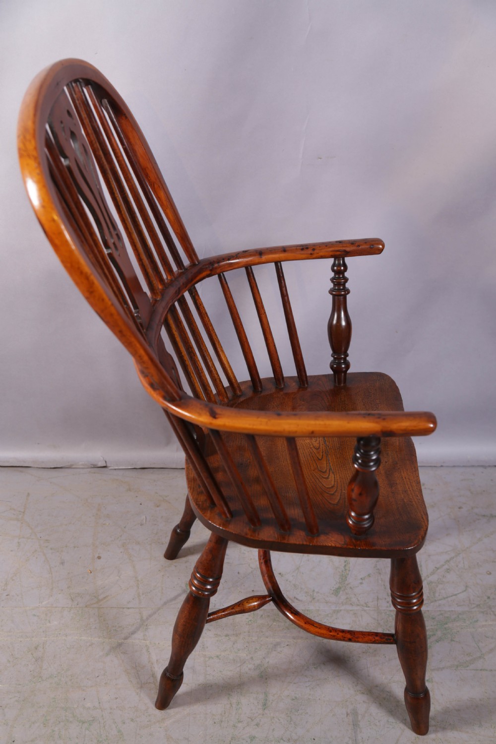 An antique yew wood high back Windsor armchair featuring a pierced central splat, spindled hoop back, turned legs, and a solid shaped seat. View II