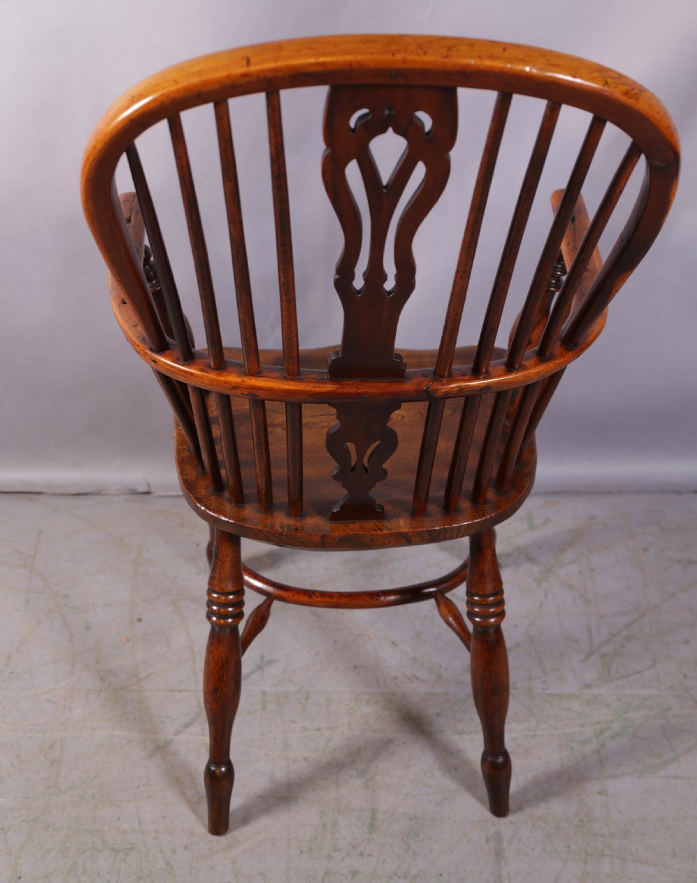 An antique yew wood high back Windsor armchair featuring a pierced central splat, spindled hoop back, turned legs, and a solid shaped seat. View III