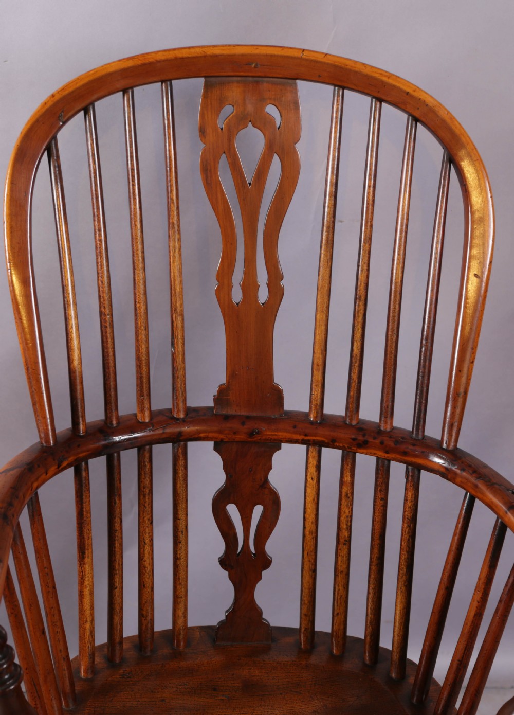 An antique yew wood high back Windsor armchair featuring a pierced central splat, spindled hoop back, turned legs, and a solid shaped seat. View V