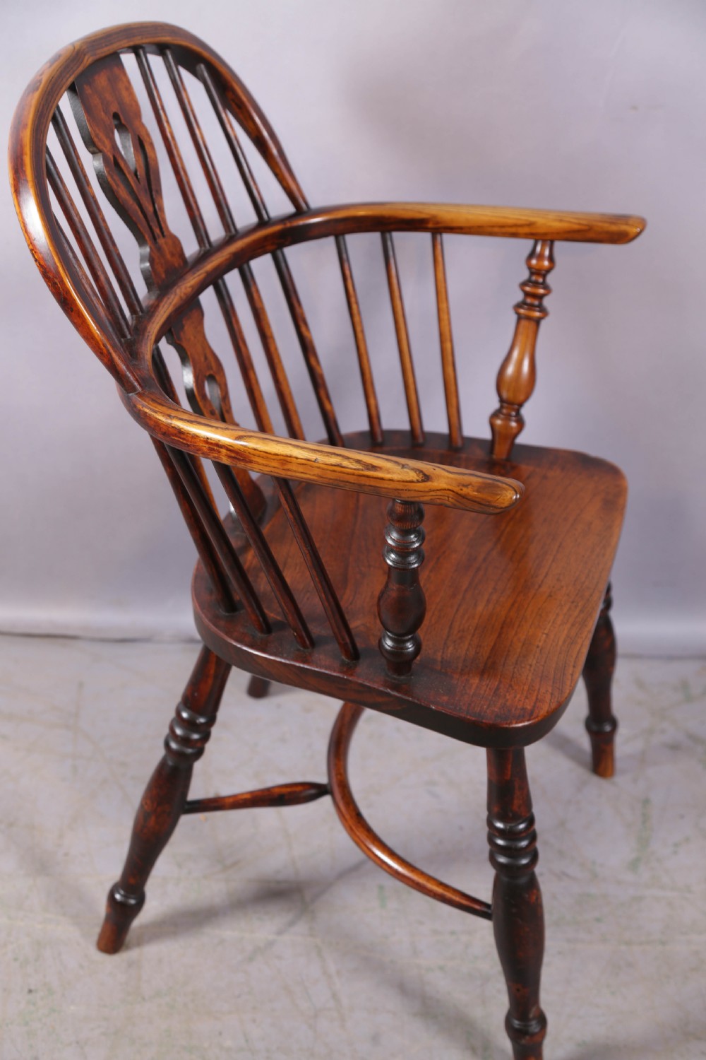 An antique ash and elm Windsor armchair featuring a steam-bent hoop back, pierced splat, turned legs, and a crinoline stretcher.