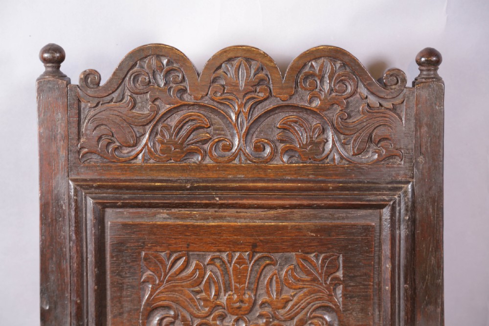 A dark oak wainscot chair featuring a carved panelled backrest, shaped scrolled arms, and turned front legs. View IV