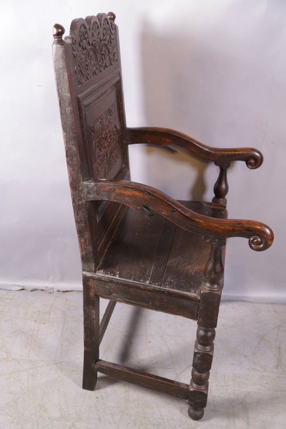 A dark oak wainscot chair featuring a carved panelled backrest, shaped scrolled arms, and turned front legs. View VII