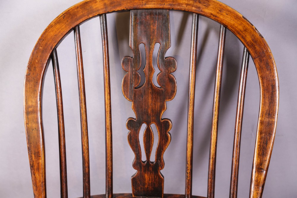 An antique high-back wooden Windsor armchair crafted from ash and elm with a pierced central splat, turned legs, and a shaped saddle seat. View X