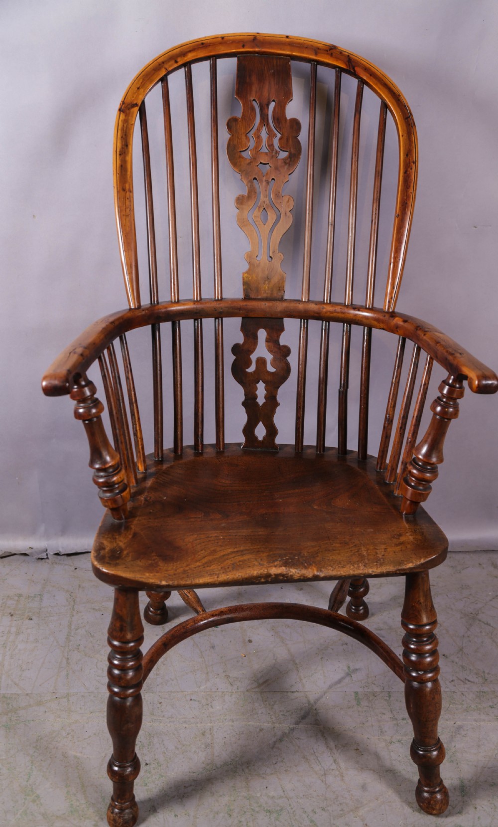 An antique yew wood Windsor armchair featuring a high hoop back, pierced fretwork central splat, turned legs, and a crinoline stretcher.