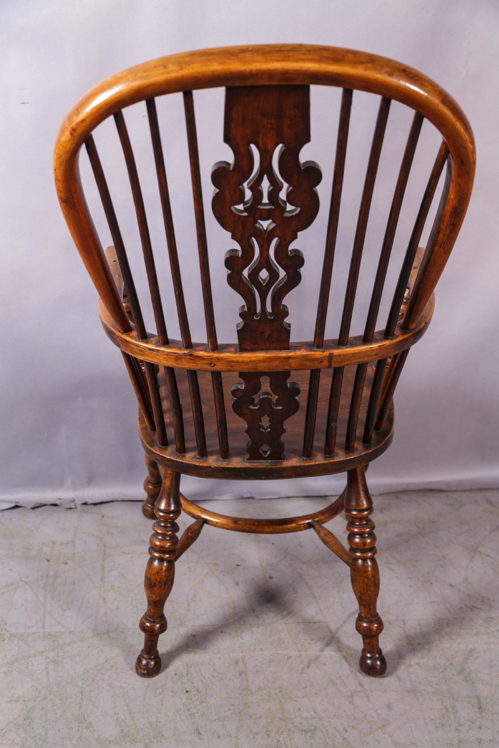 An antique yew wood Windsor armchair featuring a high hoop back, pierced fretwork central splat, turned legs, and a crinoline stretcher. View IV