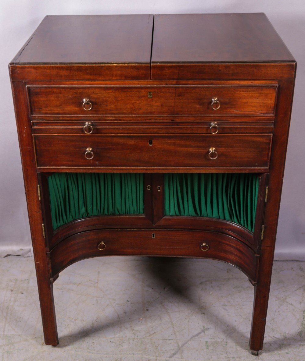 A Georgian mahogany gentlemans dressing chest featuring a split hinged top, brass ring handles, and a concave lower section with green fabric panels.