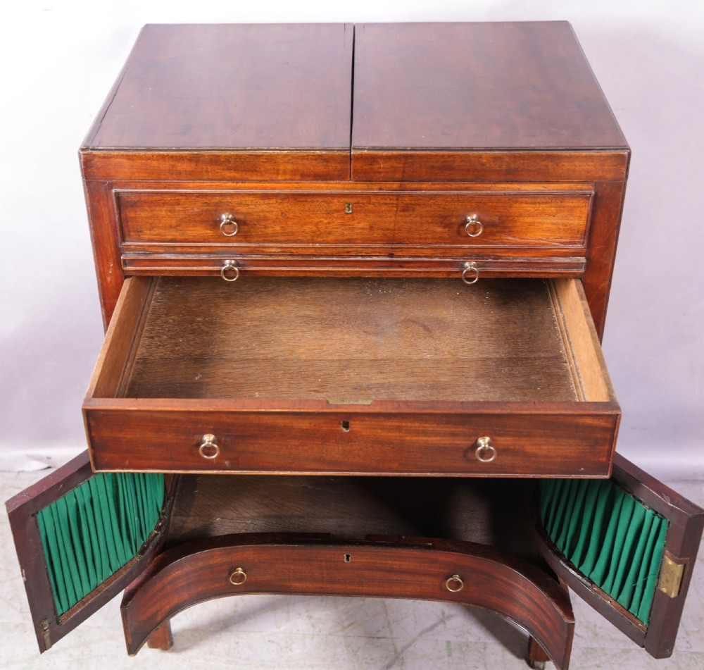 A Georgian mahogany gentlemans dressing chest featuring a split hinged top, brass ring handles, and a concave lower section with green fabric panels. View IV