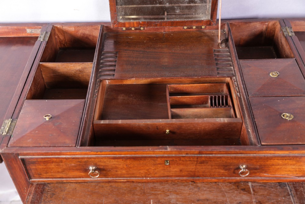 A Georgian mahogany gentlemans dressing chest featuring a split hinged top, brass ring handles, and a concave lower section with green fabric panels. View VI