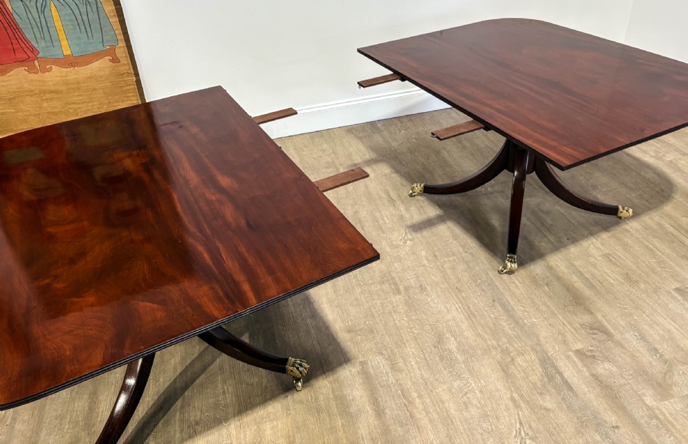 A large polished mahogany twin pedestal dining table with brass claw feet and extending leaves set on a wooden floor. View II