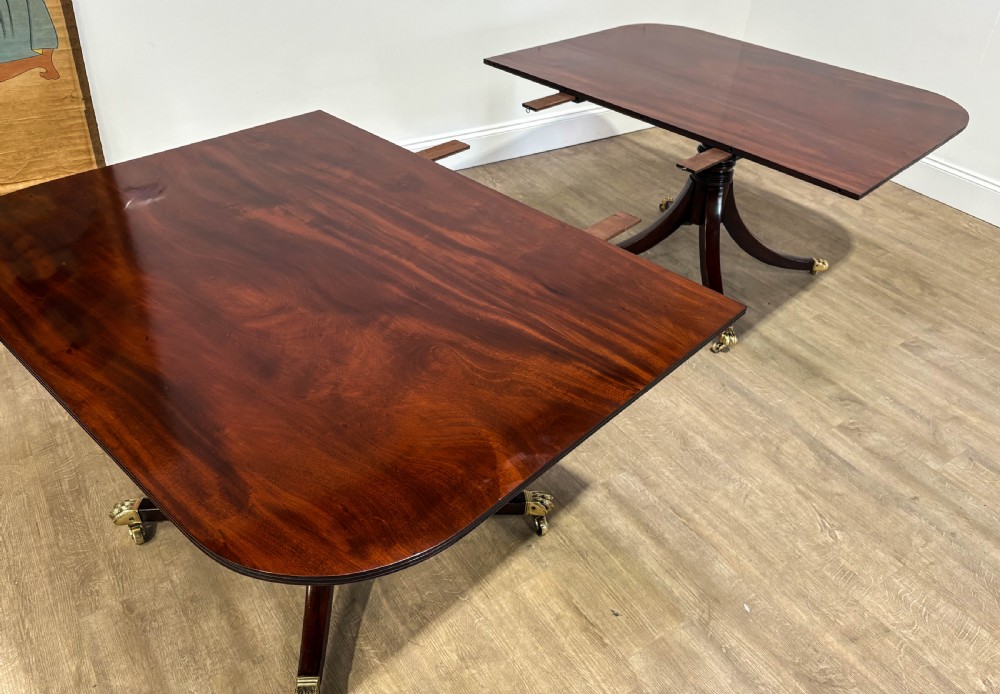 A large polished mahogany twin pedestal dining table with brass claw feet and extending leaves set on a wooden floor. View IV