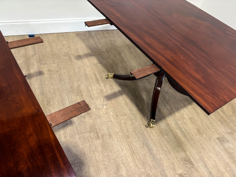 A large polished mahogany twin pedestal dining table with brass claw feet and extending leaves set on a wooden floor. View VI