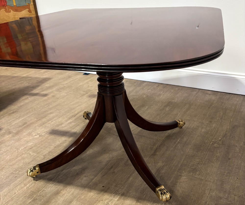 A large polished mahogany twin pedestal dining table with brass claw feet and extending leaves set on a wooden floor. View IX