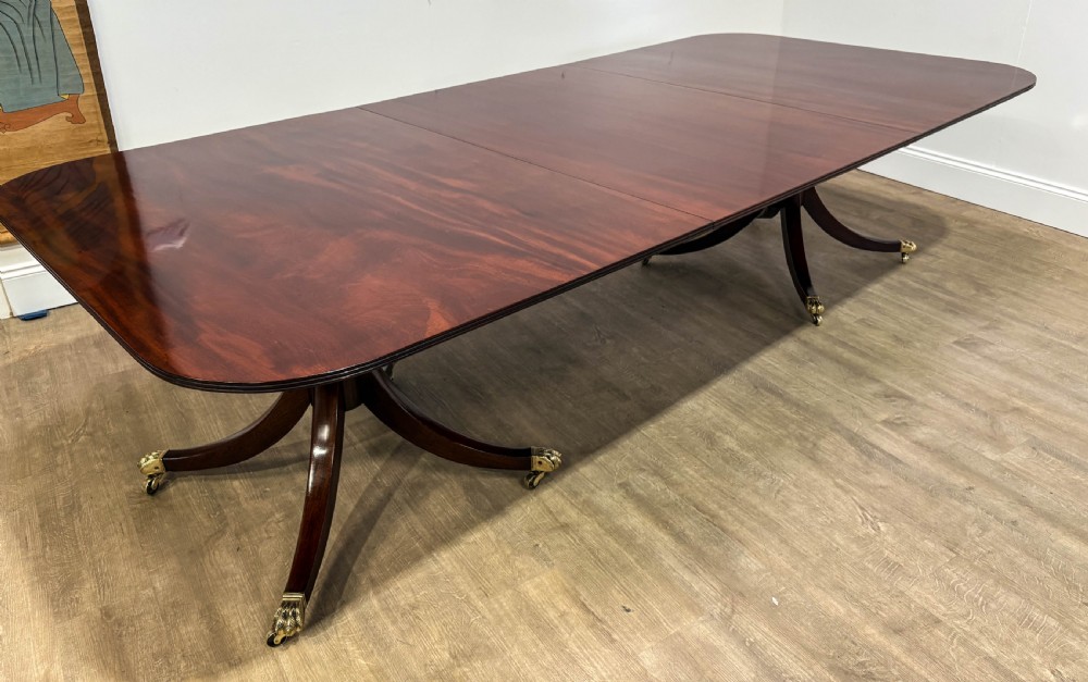 A large polished mahogany twin pedestal dining table with brass claw feet and extending leaves set on a wooden floor. View XI