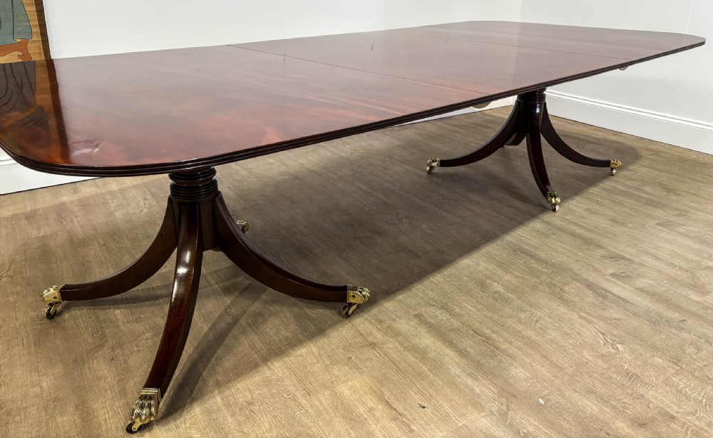 A large polished mahogany twin pedestal dining table with brass claw feet and extending leaves set on a wooden floor. View XII