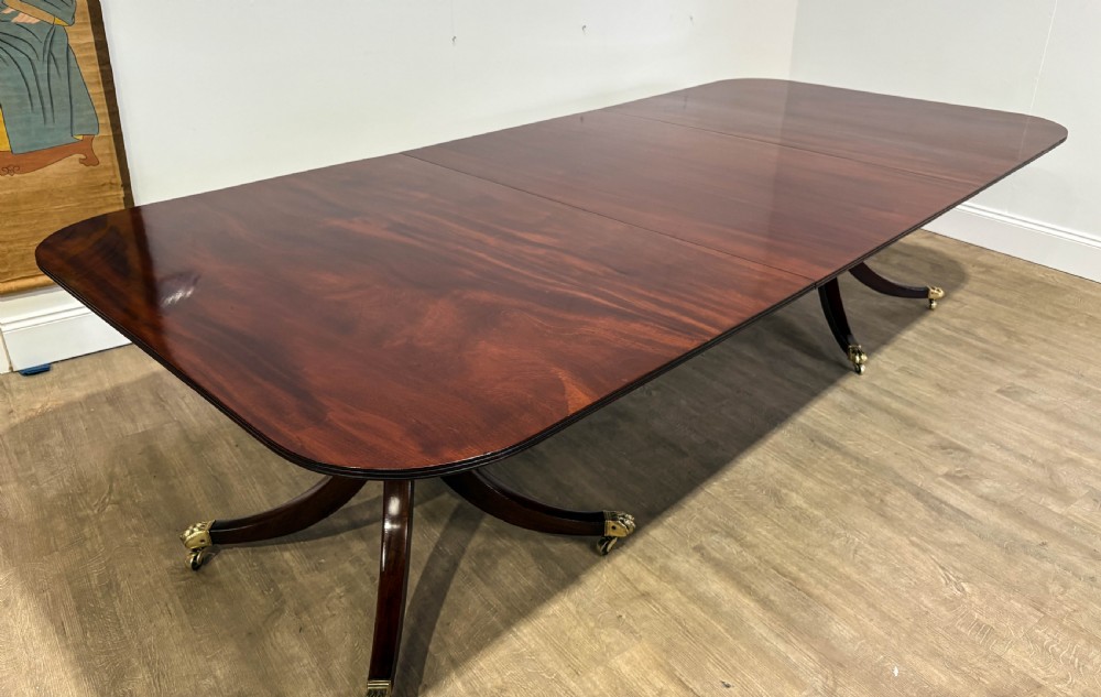 A large polished mahogany twin pedestal dining table with brass claw feet and extending leaves set on a wooden floor. View XXV
