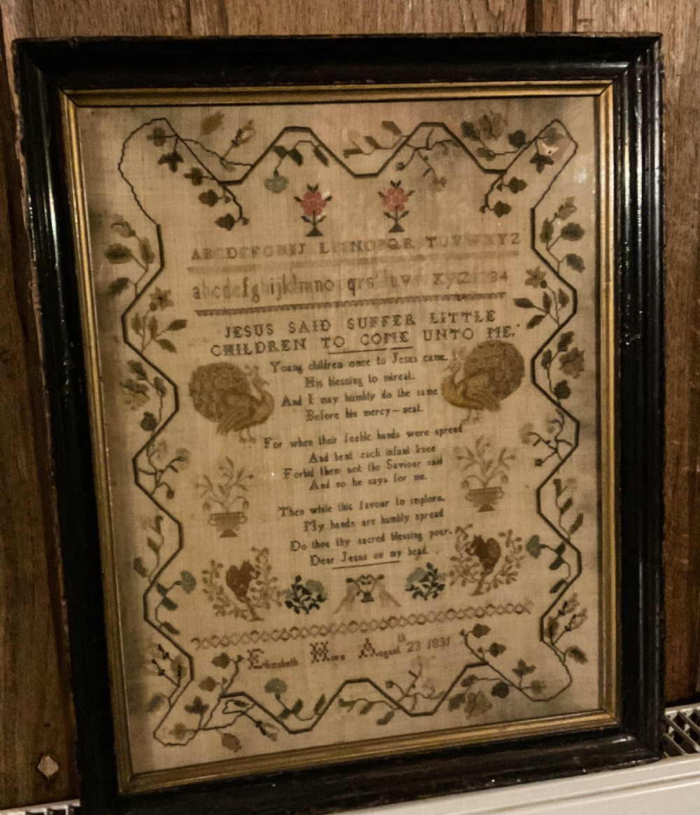 Framed 1831 needlework sampler featuring an embroidered alphabet, religious verse, peacocks, floral borders, and a signature dated August 23 1831.