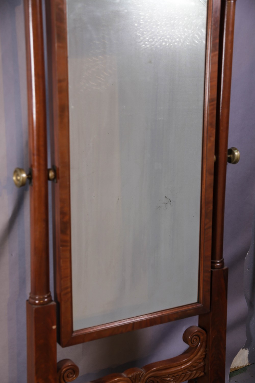 An American Empire mahogany cheval mirror with turned side columns, a pedimented top, brass mounts, and a carved scroll base with paw feet. View VII