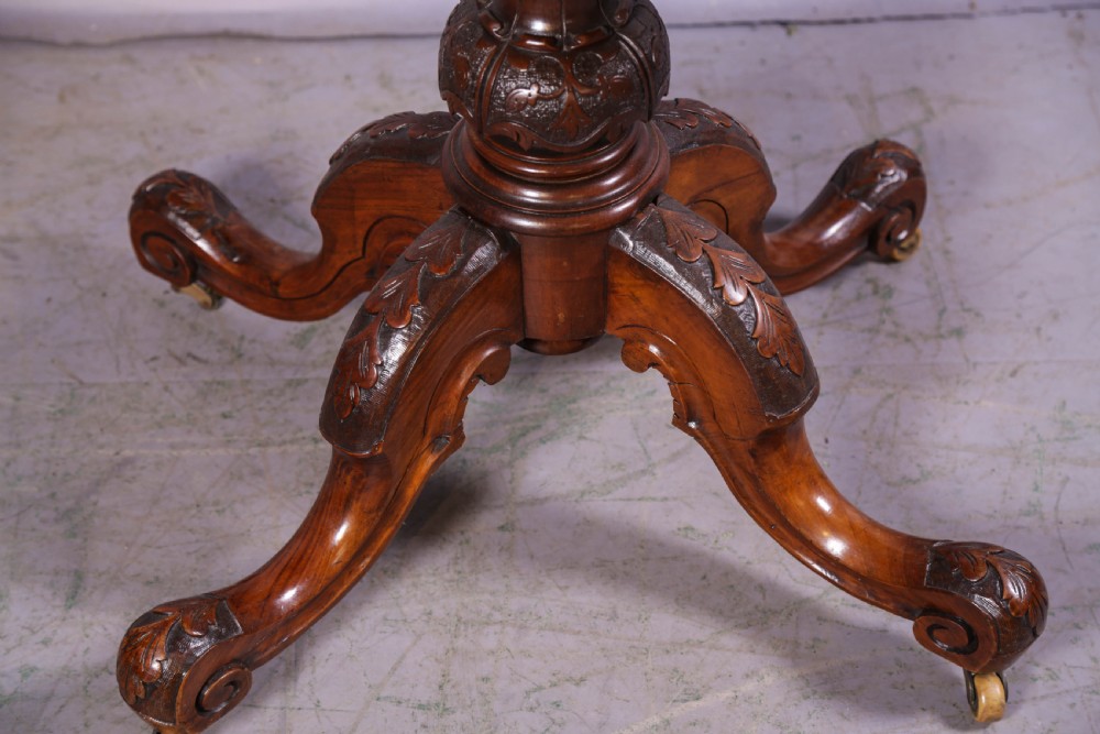 A Victorian burr walnut fold-over card table featuring a shaped top, a carved pedestal stem, and carved quadripartite cabriole legs on brass castors. View III