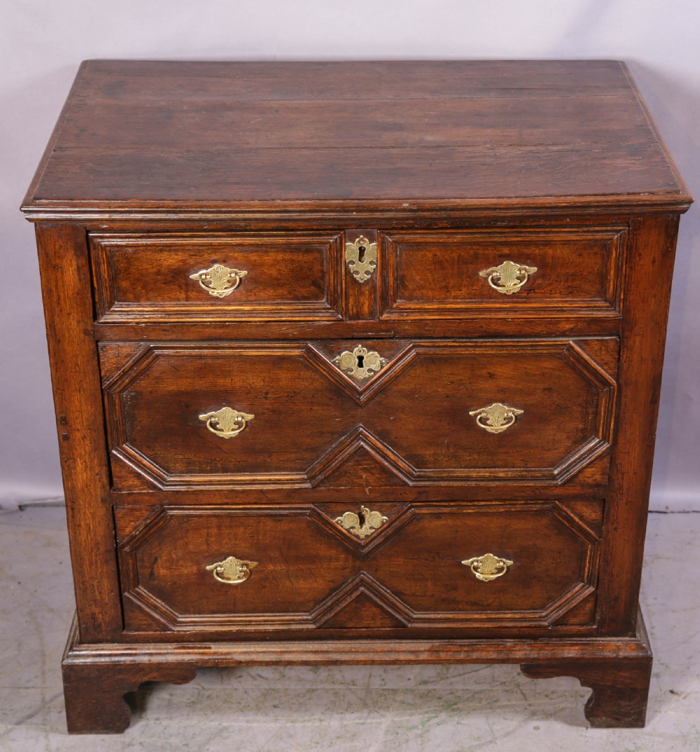 An early 18th-century dark oak chest of drawers featuring geometric moulding on the drawer fronts and brass drop handles. View IV