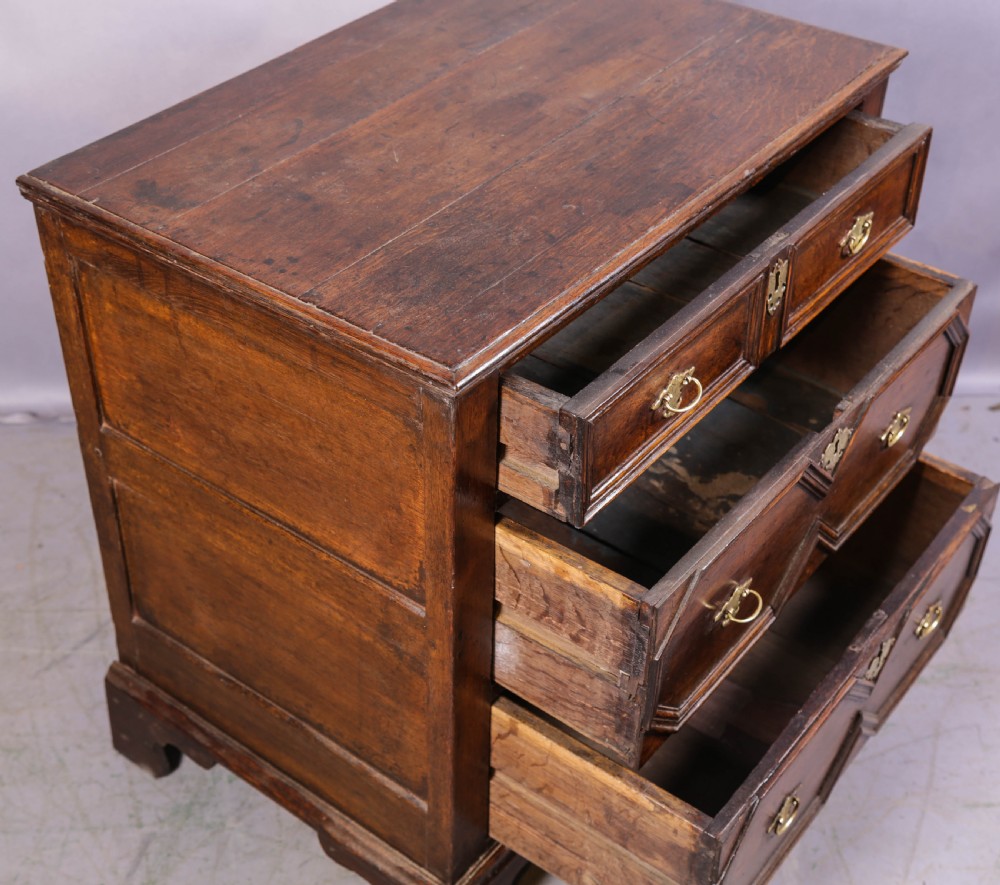 An early 18th-century dark oak chest of drawers featuring geometric moulding on the drawer fronts and brass drop handles. View VII