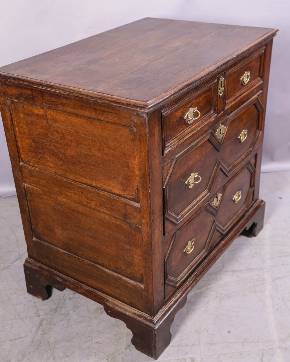 An early 18th-century dark oak chest of drawers featuring geometric moulding on the drawer fronts and brass drop handles. View VIII
