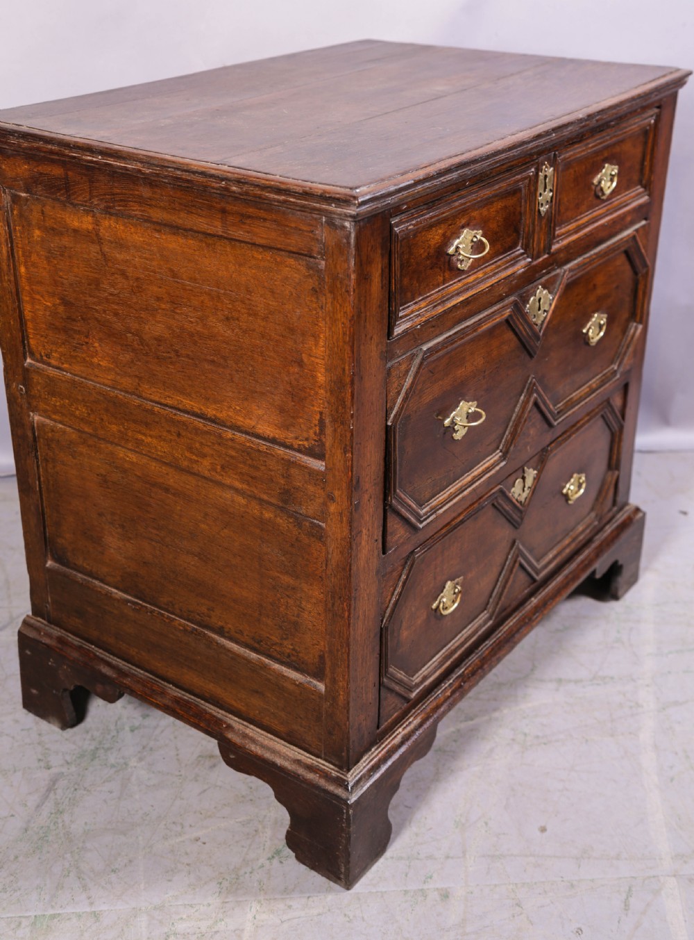 An early 18th-century dark oak chest of drawers featuring geometric moulding on the drawer fronts and brass drop handles. View IX