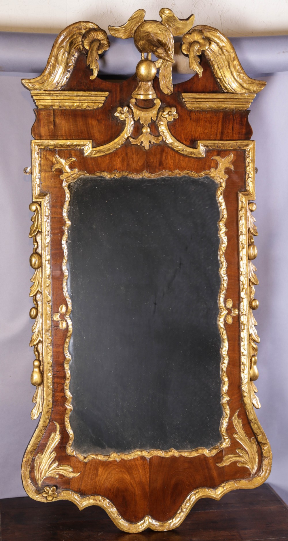 An 18th-century pier glass featuring a walnut veneer frame with elaborate giltwood carvings, scroll pediment, and a central carved eagle cresting.