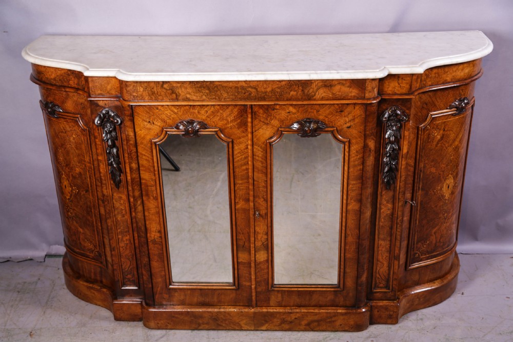 A serpentine-fronted Victorian burr walnut credenza featuring a white marble top, mirrored doors, and carved wooden mounts. View II