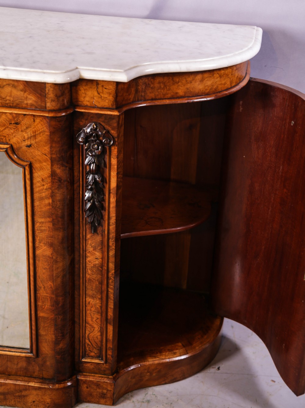 A serpentine-fronted Victorian burr walnut credenza featuring a white marble top, mirrored doors, and carved wooden mounts. View III