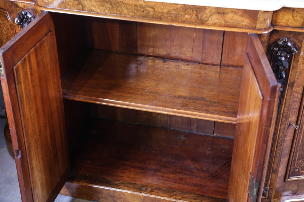 A serpentine-fronted Victorian burr walnut credenza featuring a white marble top, mirrored doors, and carved wooden mounts. View V