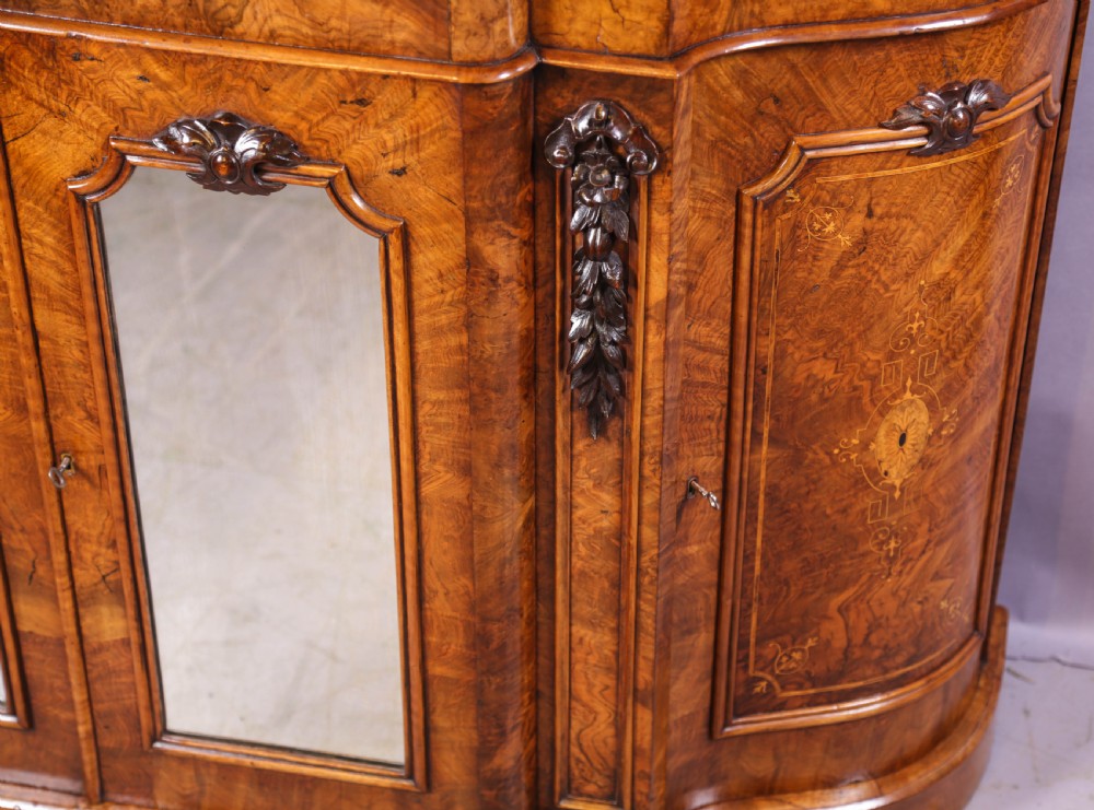 A serpentine-fronted Victorian burr walnut credenza featuring a white marble top, mirrored doors, and carved wooden mounts. View VIII