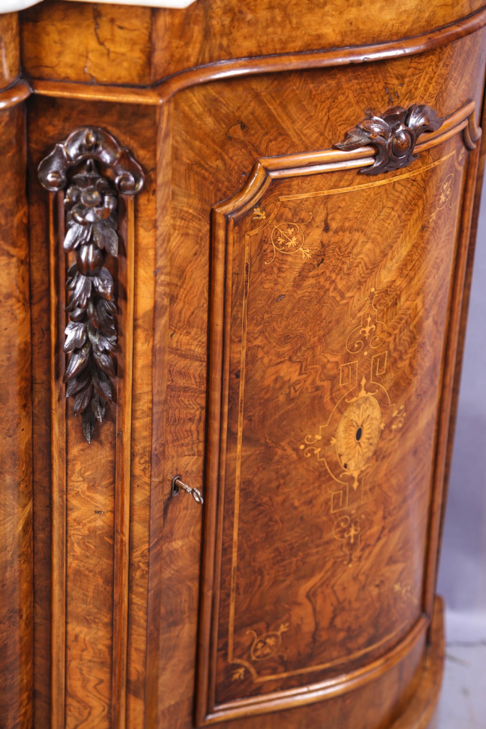 A serpentine-fronted Victorian burr walnut credenza featuring a white marble top, mirrored doors, and carved wooden mounts. View IX