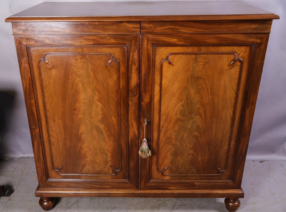 A 19th-century flame mahogany two-door estate cabinet with carved spandrel mouldings and turned bun feet.