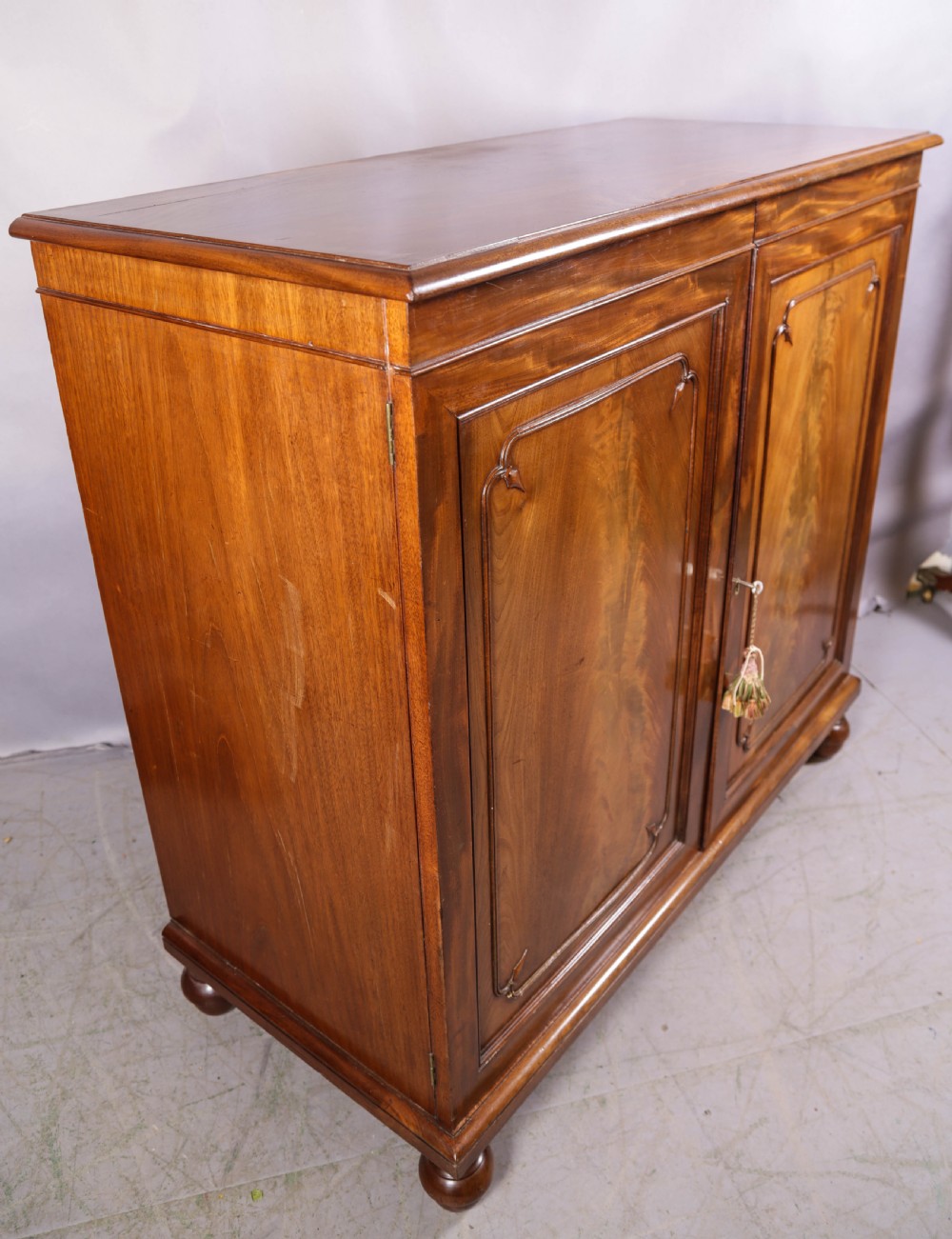 A 19th-century flame mahogany two-door estate cabinet with carved spandrel mouldings and turned bun feet. View II