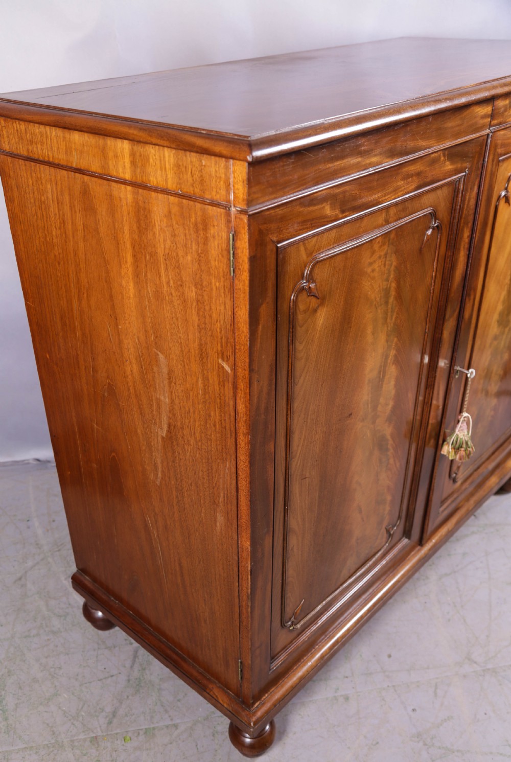 A 19th-century flame mahogany two-door estate cabinet with carved spandrel mouldings and turned bun feet. View III