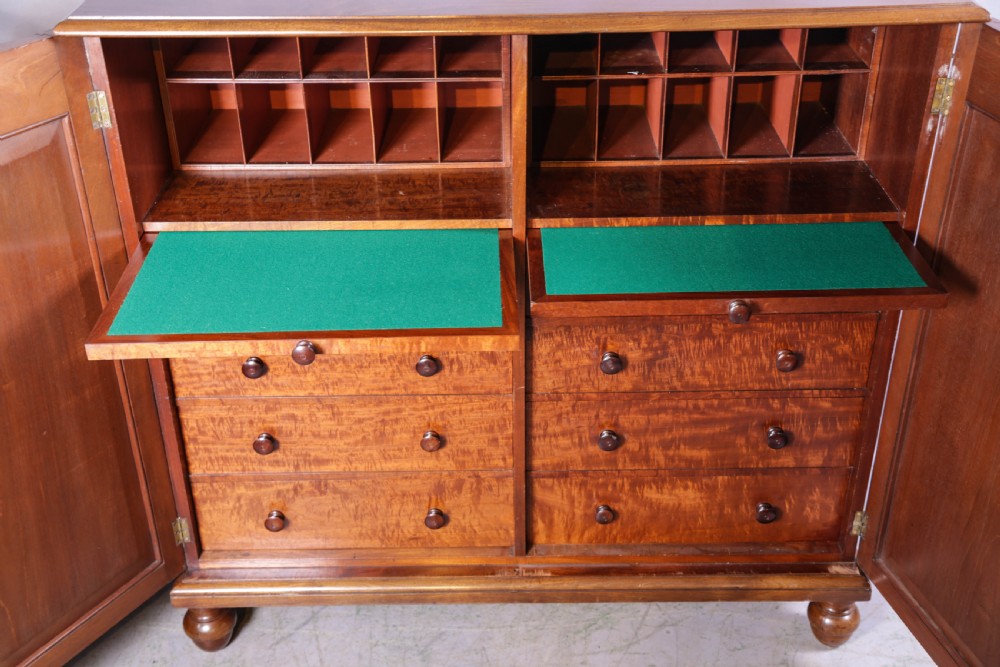 A 19th-century flame mahogany two-door estate cabinet with carved spandrel mouldings and turned bun feet. View VII