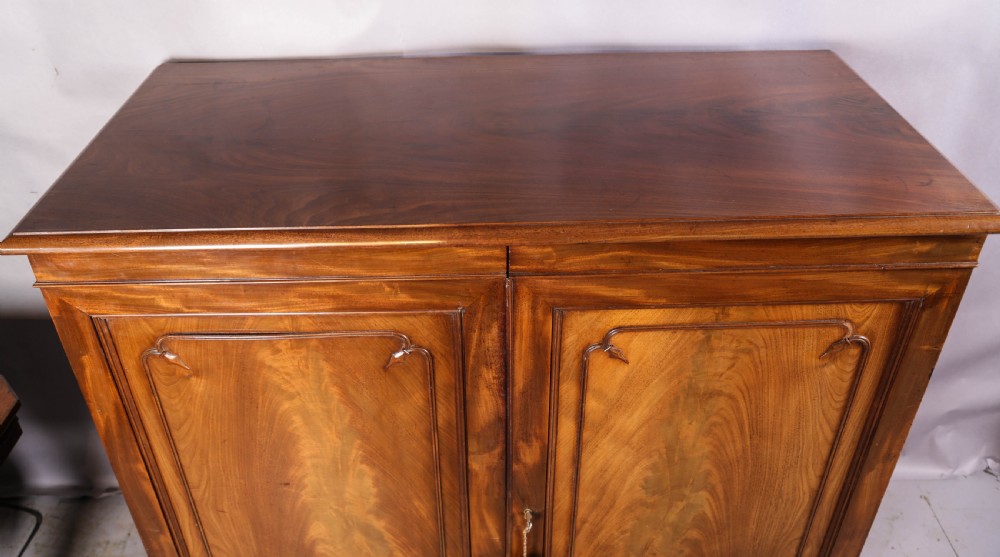 A 19th-century flame mahogany two-door estate cabinet with carved spandrel mouldings and turned bun feet. View XIII