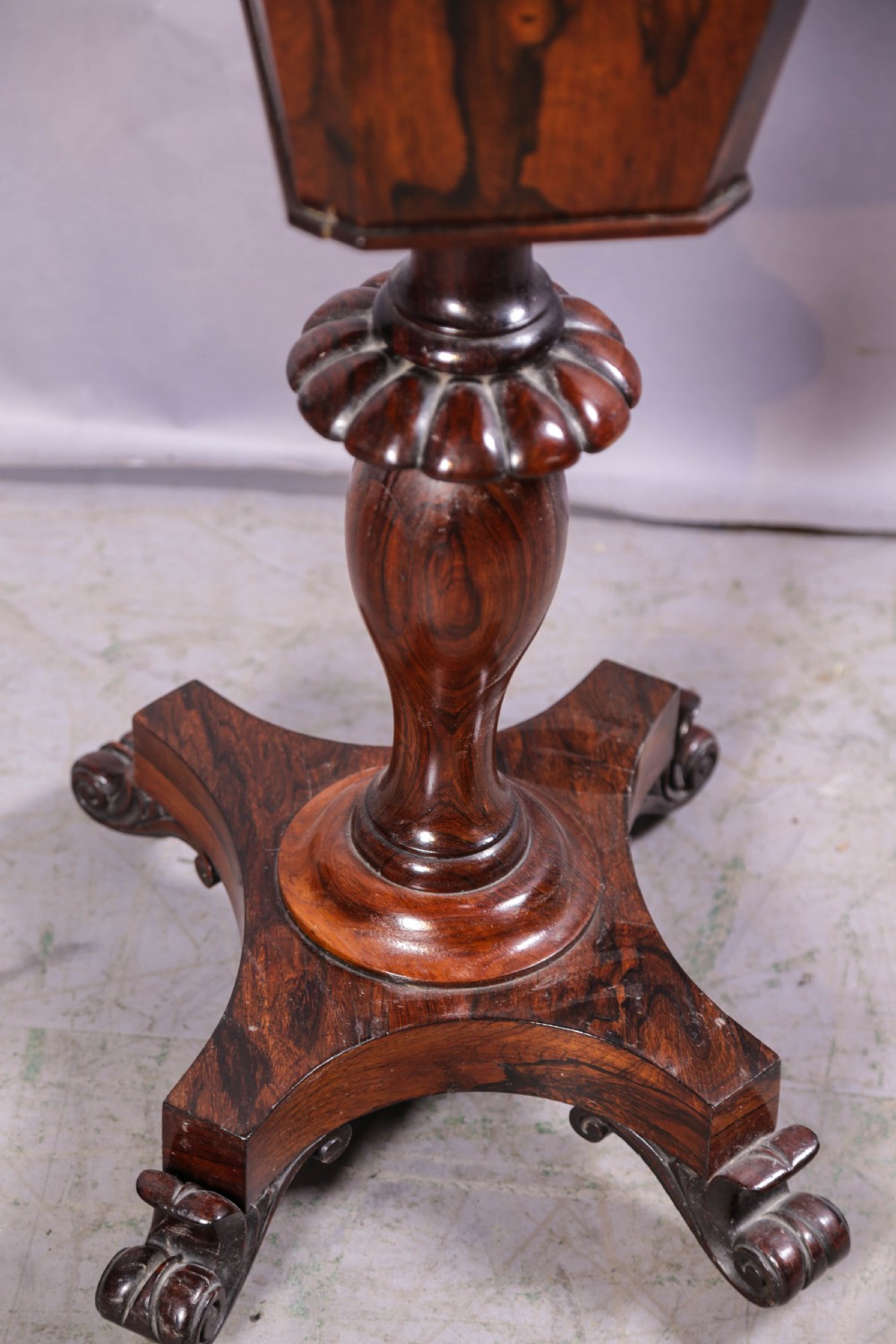 An octagonal Victorian rosewood sewing stand with a tapered compartment, a carved pedestal base, and scrolling feet on castors. View VII