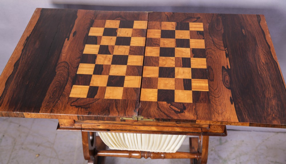A Victorian rosewood sewing and games table featuring a fold-over top, a single frieze drawer, and a suspended pleated fabric work bag supported by a lyre-form pedestal base with brass castors. View III