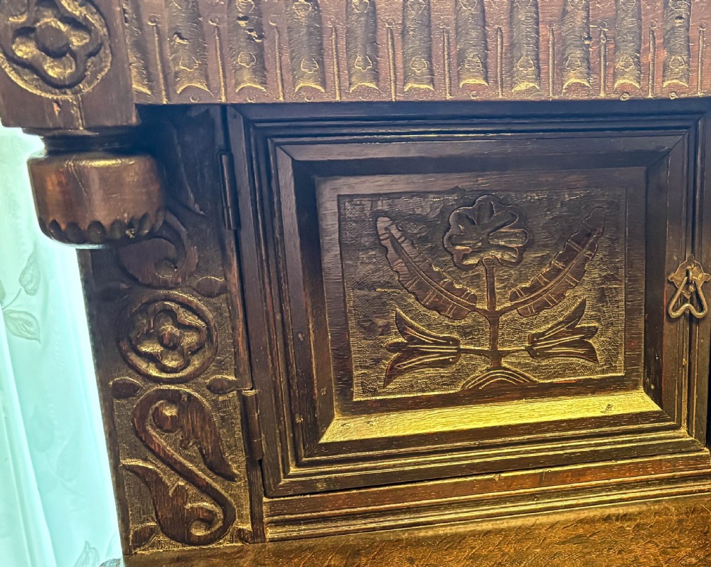 A front view of a dark brown antique oak livery cupboard featuring elaborate hand-carved geometric panels, friezes, and cupboard doors. View III