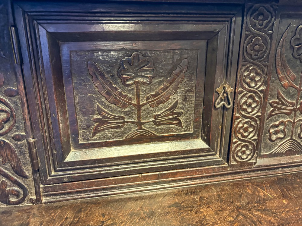 A front view of a dark brown antique oak livery cupboard featuring elaborate hand-carved geometric panels, friezes, and cupboard doors. View IV