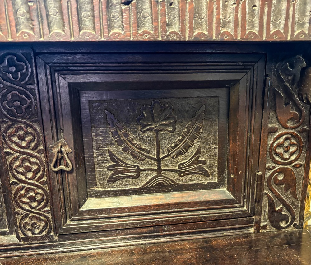 A front view of a dark brown antique oak livery cupboard featuring elaborate hand-carved geometric panels, friezes, and cupboard doors. View V