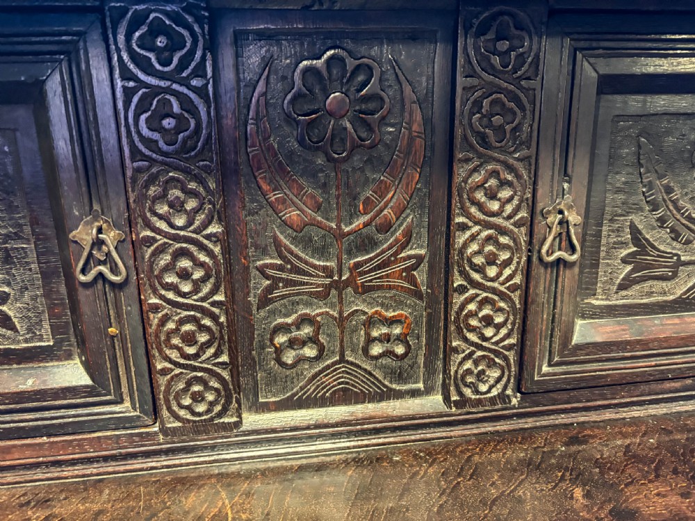 A front view of a dark brown antique oak livery cupboard featuring elaborate hand-carved geometric panels, friezes, and cupboard doors. View VI