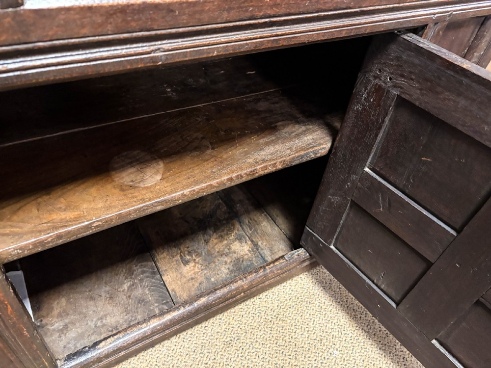 A front view of a dark brown antique oak livery cupboard featuring elaborate hand-carved geometric panels, friezes, and cupboard doors. View X