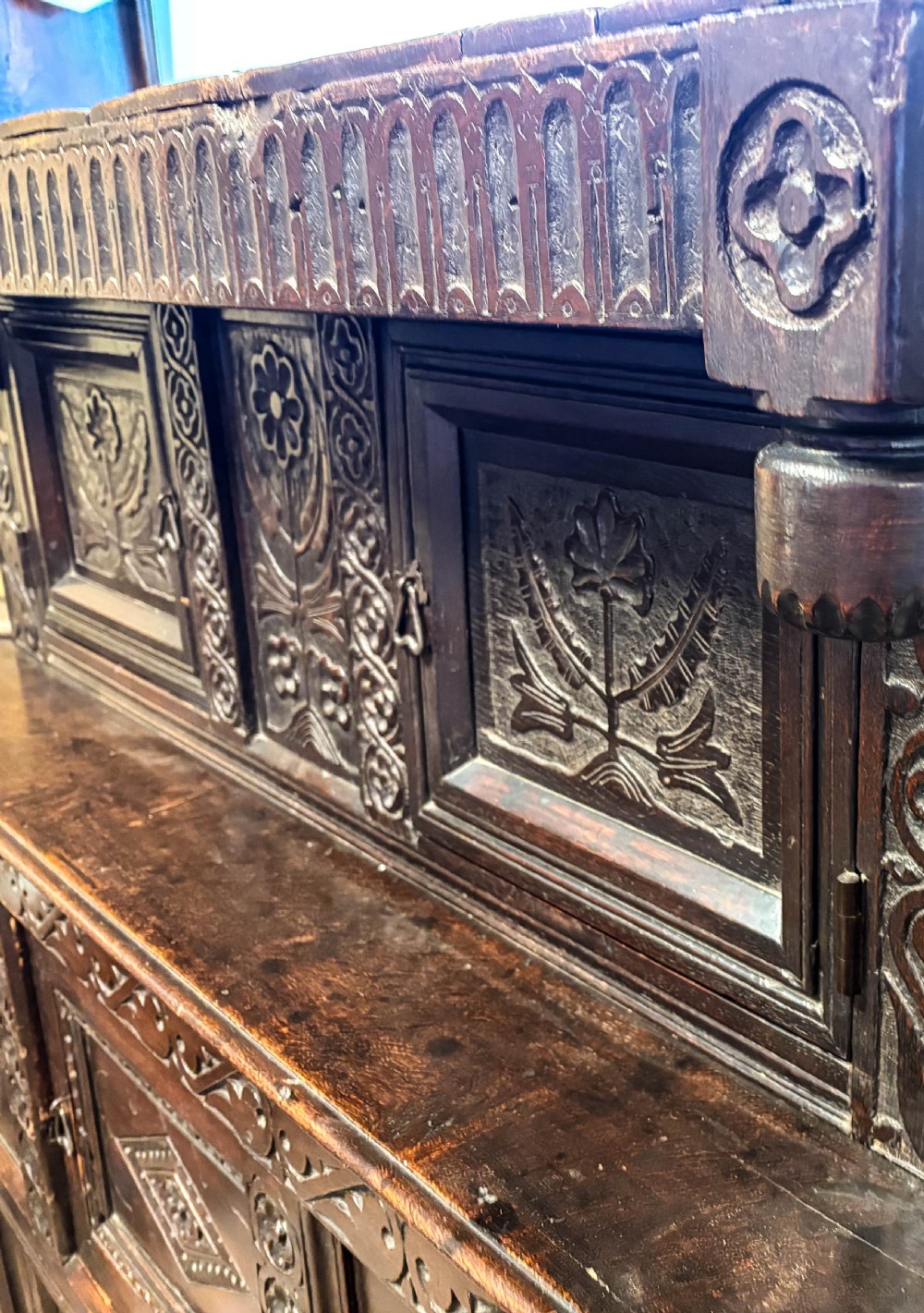 A front view of a dark brown antique oak livery cupboard featuring elaborate hand-carved geometric panels, friezes, and cupboard doors. View XII