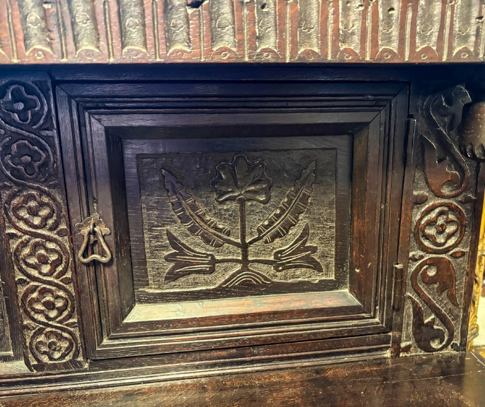 A front view of a dark brown antique oak livery cupboard featuring elaborate hand-carved geometric panels, friezes, and cupboard doors. View XVI