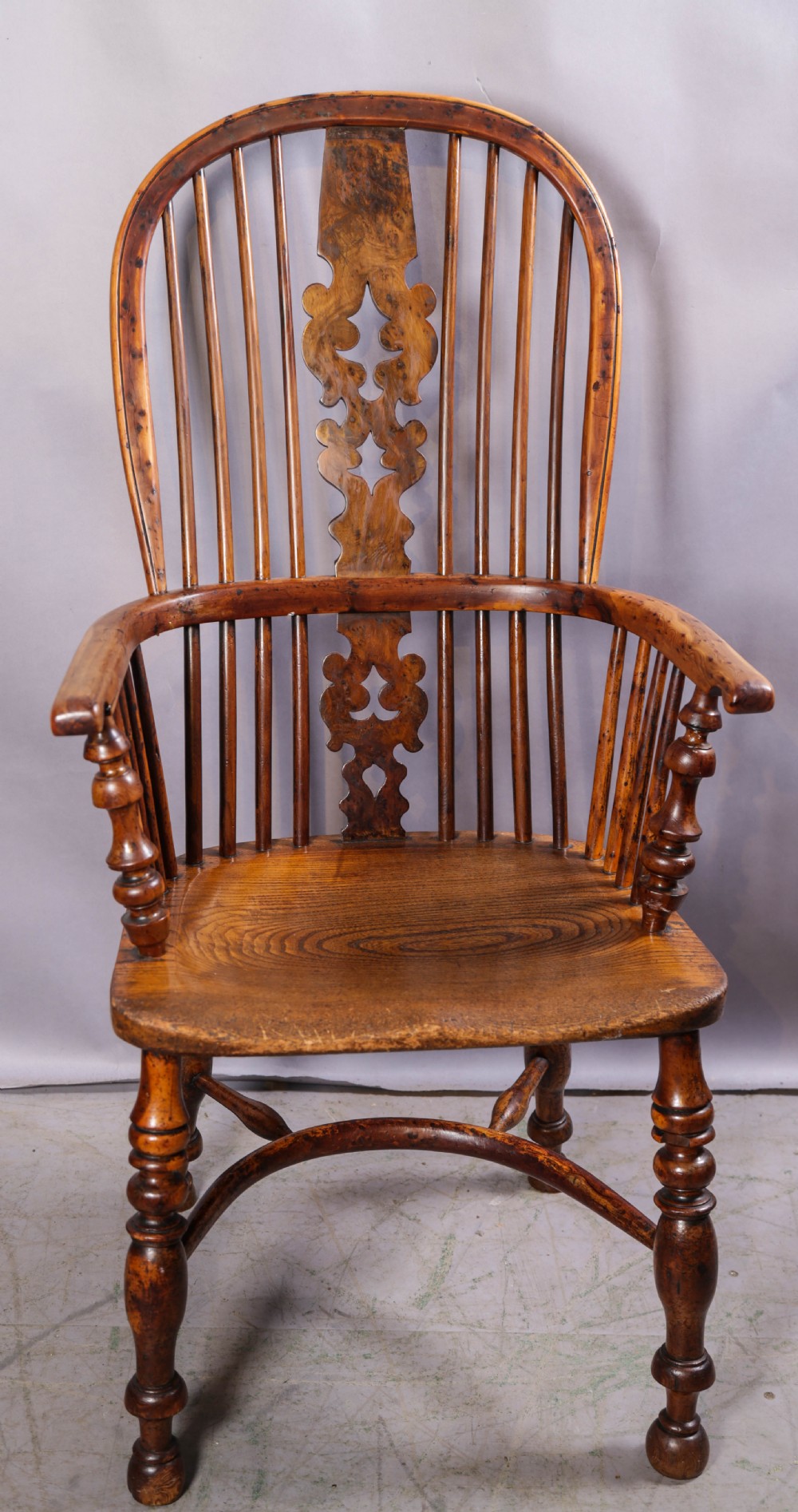 An antique yew wood high back Windsor armchair featuring a bow back, pierced central splat, shaped saddle seat, turned arm supports, turned legs, and a crinoline stretcher.