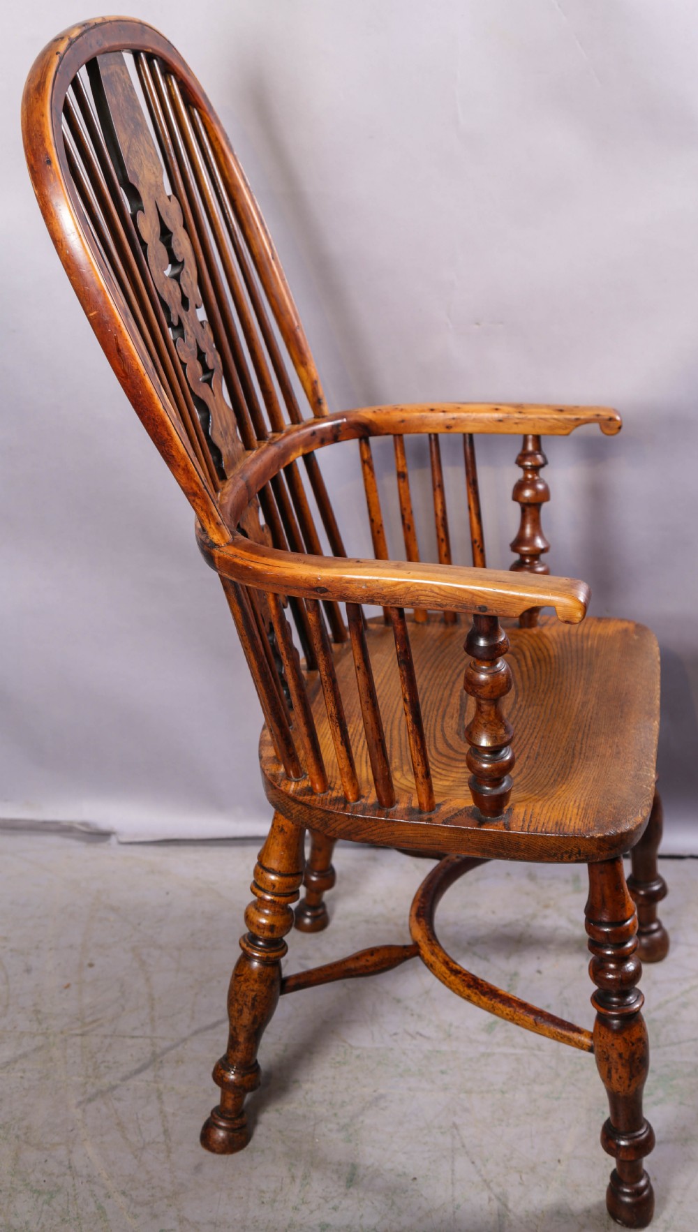 An antique yew wood high back Windsor armchair featuring a bow back, pierced central splat, shaped saddle seat, turned arm supports, turned legs, and a crinoline stretcher. View II